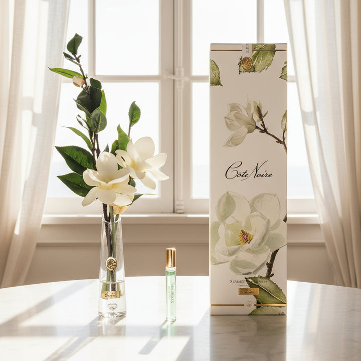 Vase with cote noire diffuser magnolias, perfume bottle, and packaging with floral design.