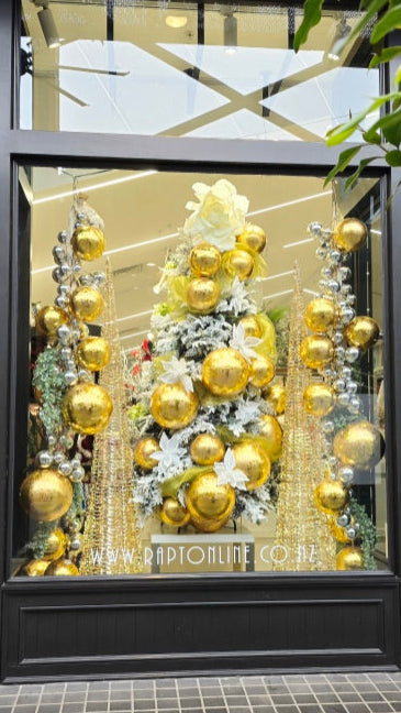 Decorative Christmas tree with gold ornaments in a store window display.