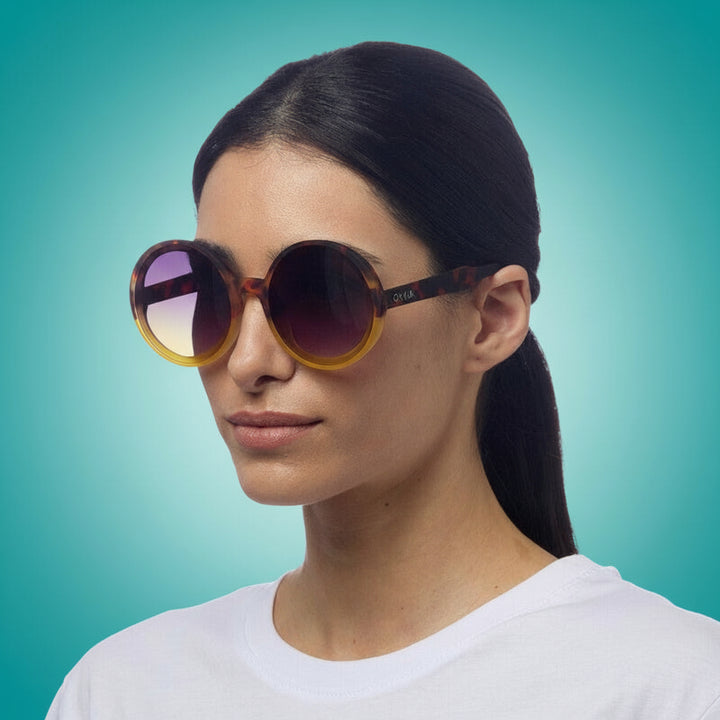 Woman wearing large round okkia sunglasses with a plain background