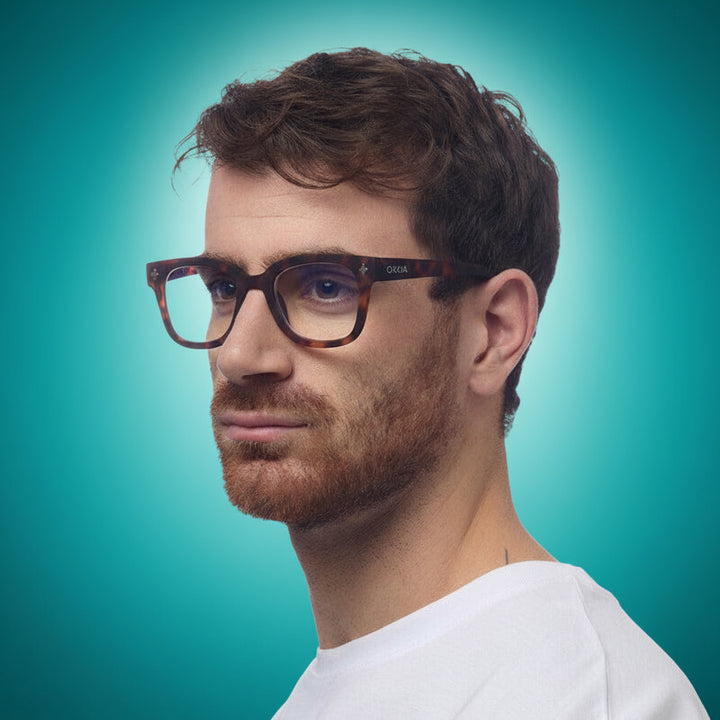 Man wearing okkia reader glasses with a turuoise background