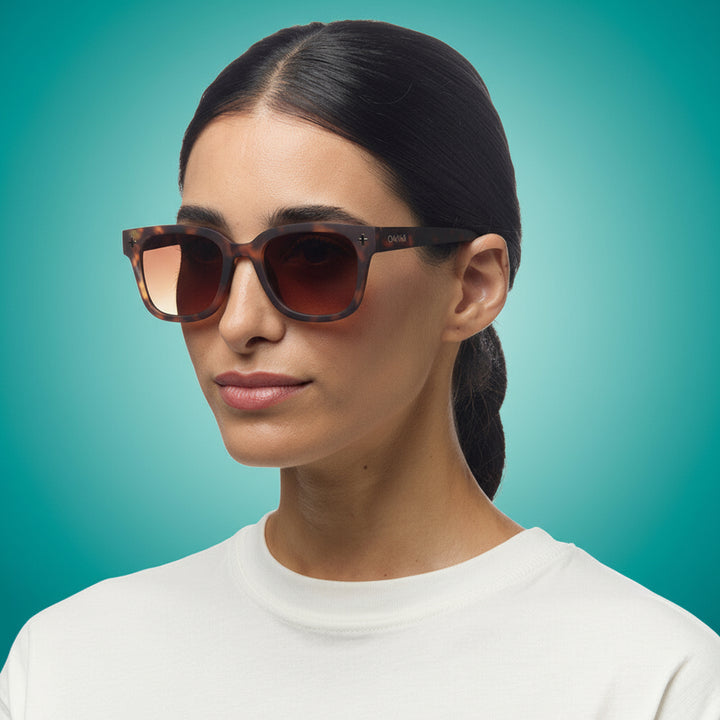 Woman wearing tortoiseshell okkia sunglasses with a plain background