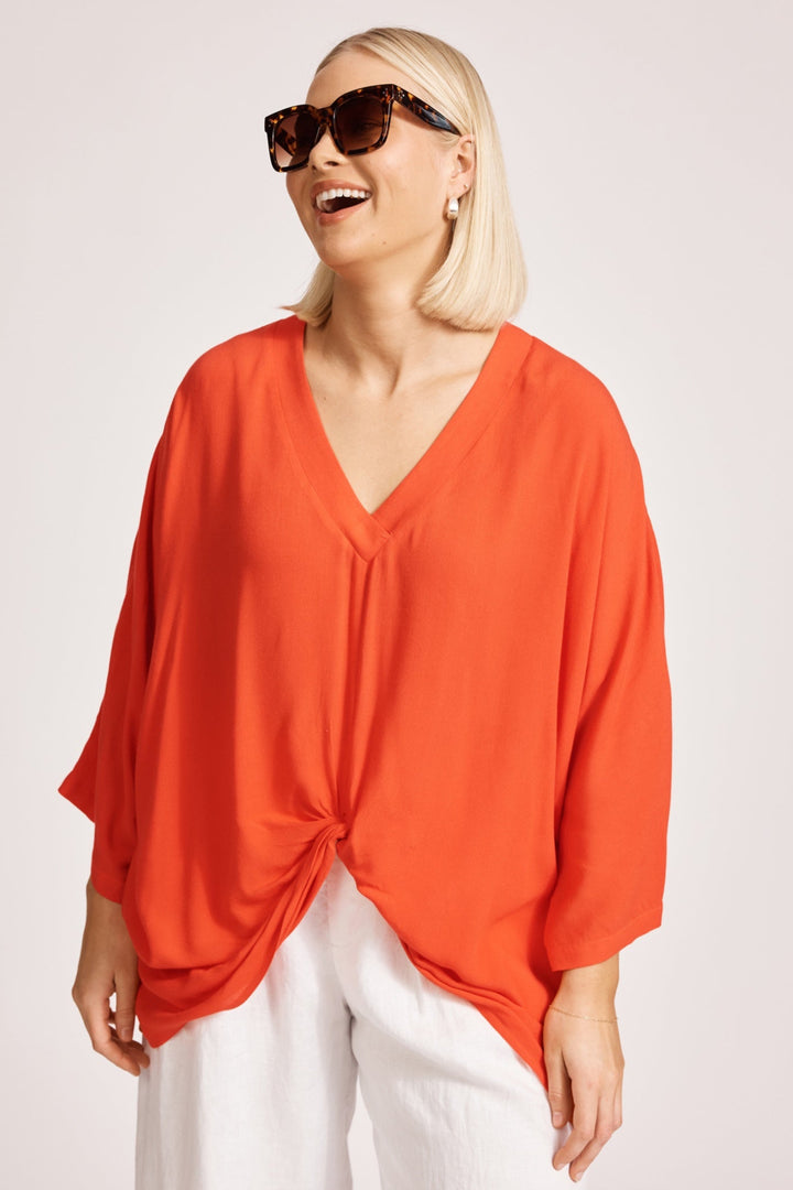 Woman wearing an orange top and sunglasses on a plain background