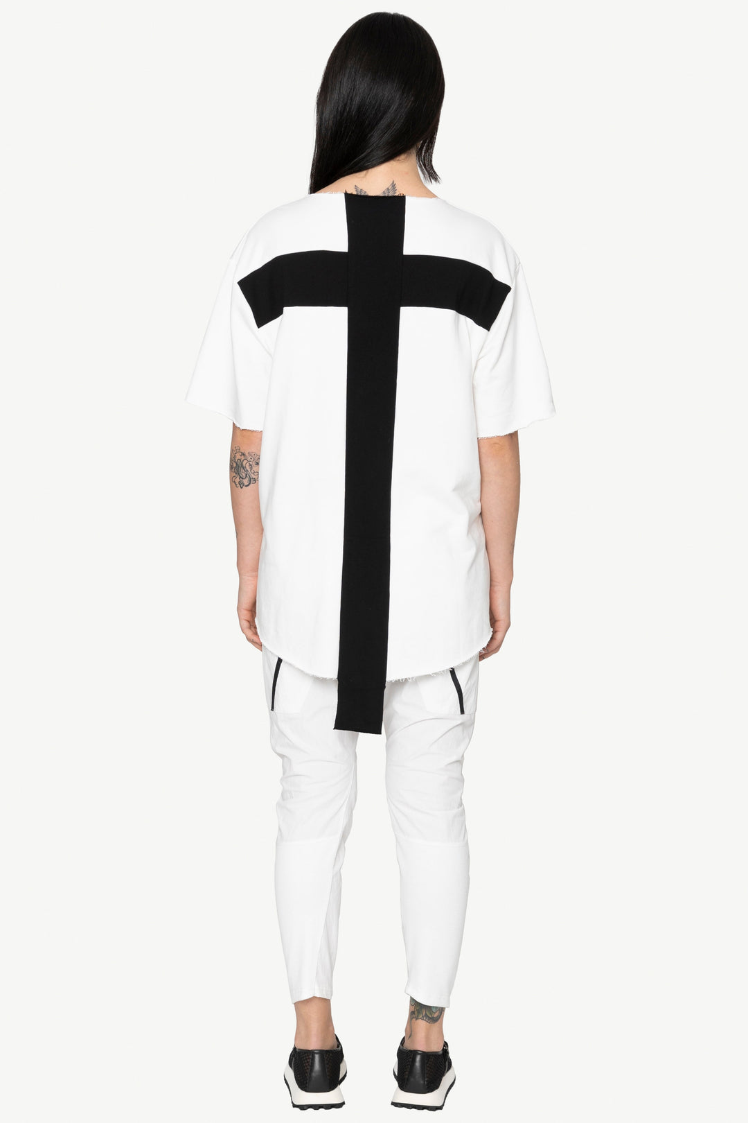 Person wearing a white outfit with a black cross design on a plain background