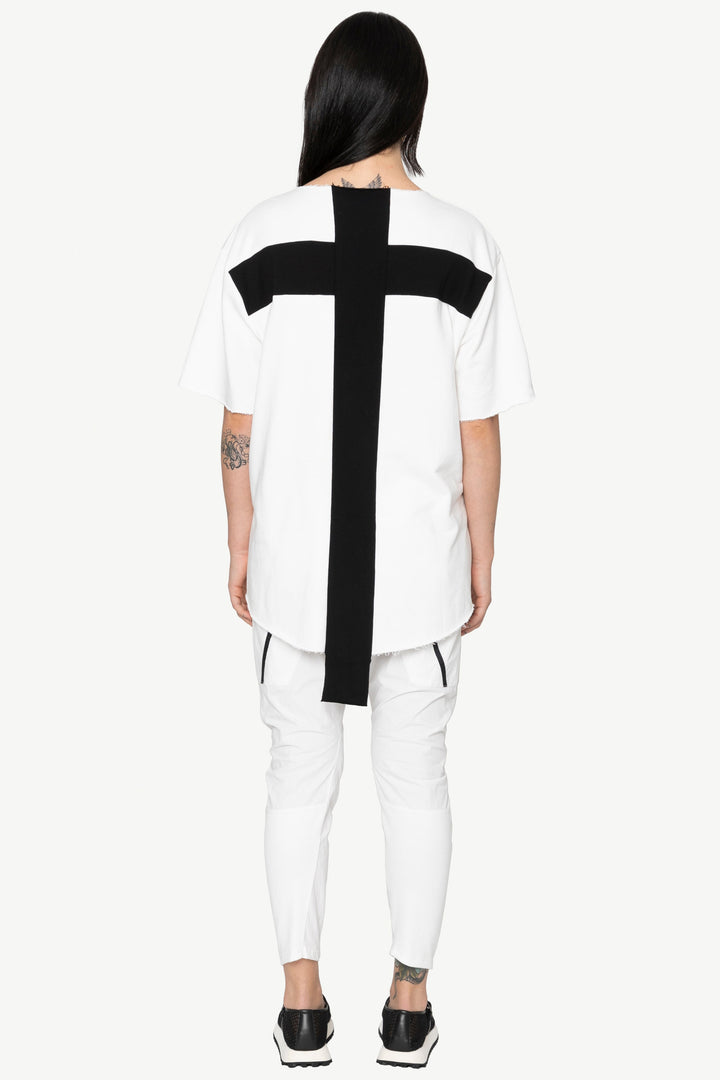 Person wearing a white outfit with a black cross design on a plain background