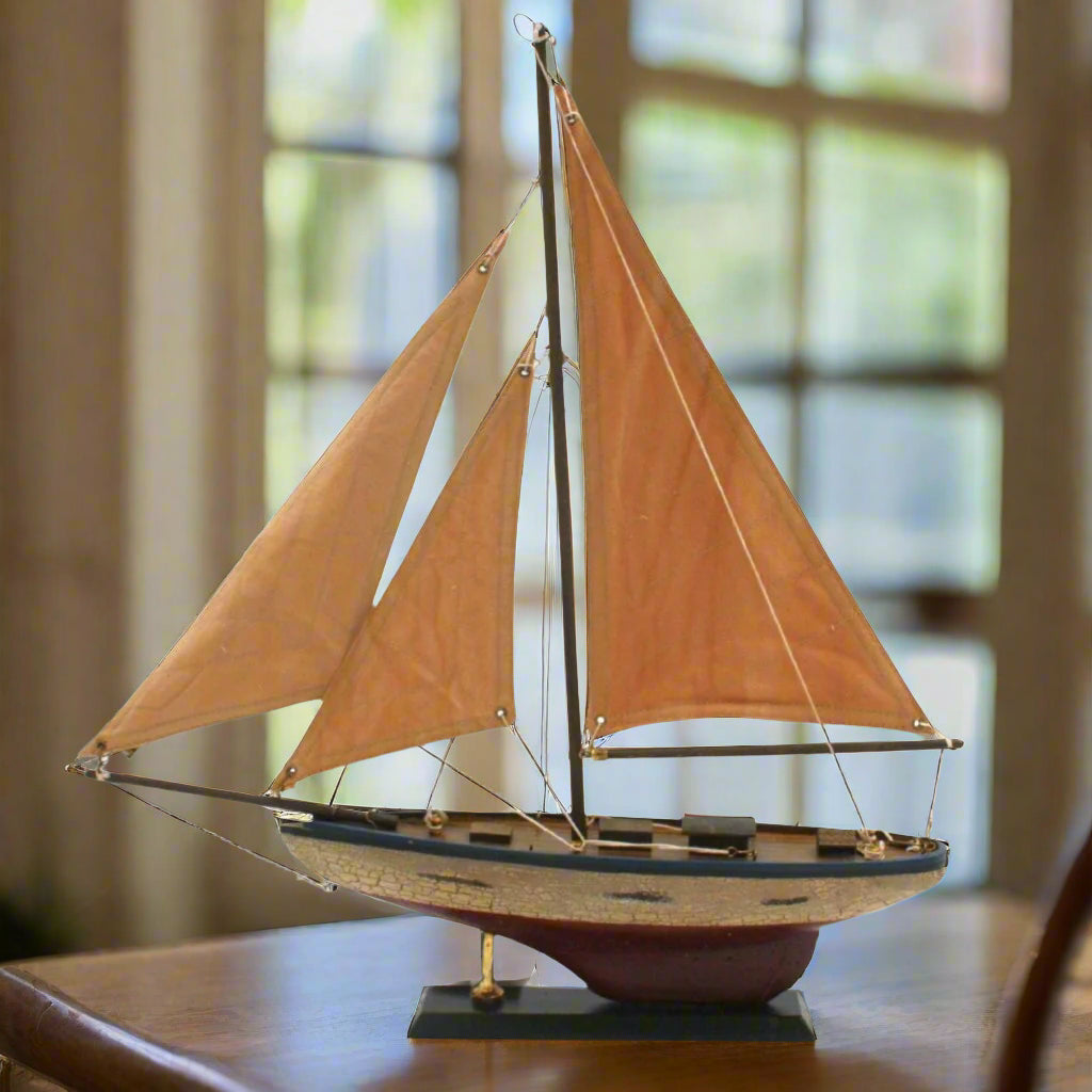 A model of a small decorative yacht made of brass and glass, displayed on a base, with a shadow falling over it.