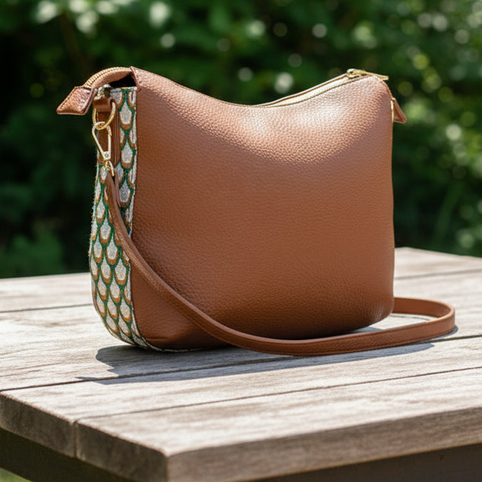 Brown leather handbag with a patterned strap on a white background