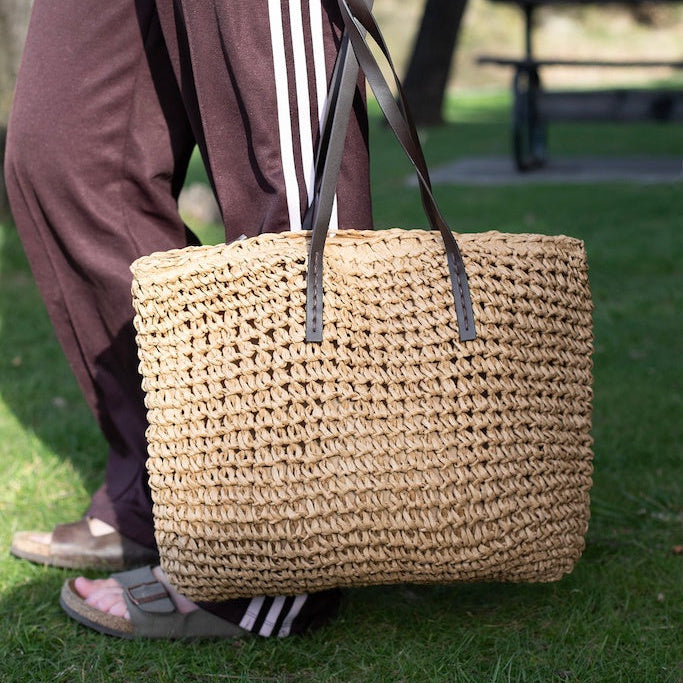 Person holding a woven bag outdoors on grass