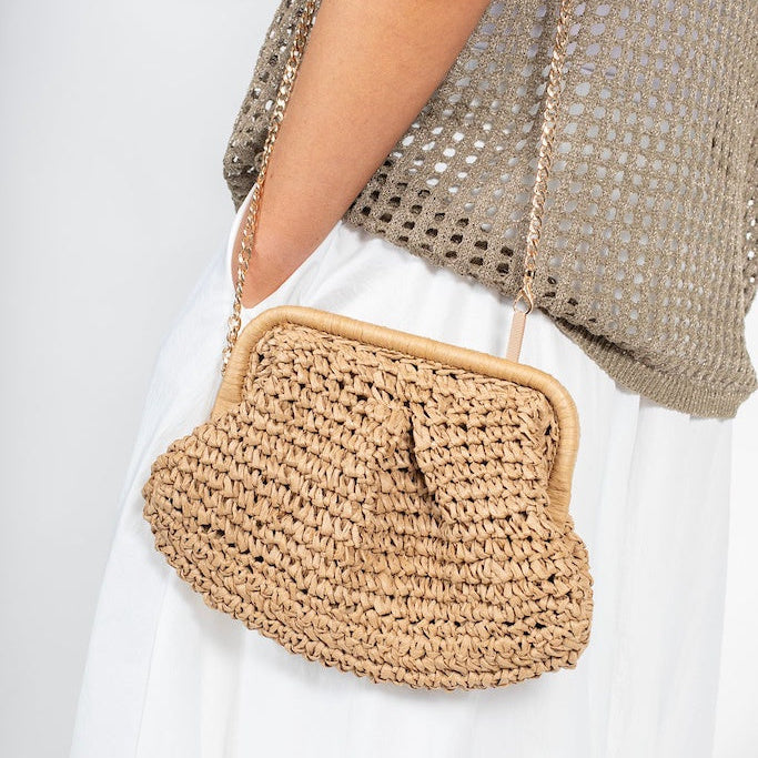 Person wearing a woven beige handbag with a plain background