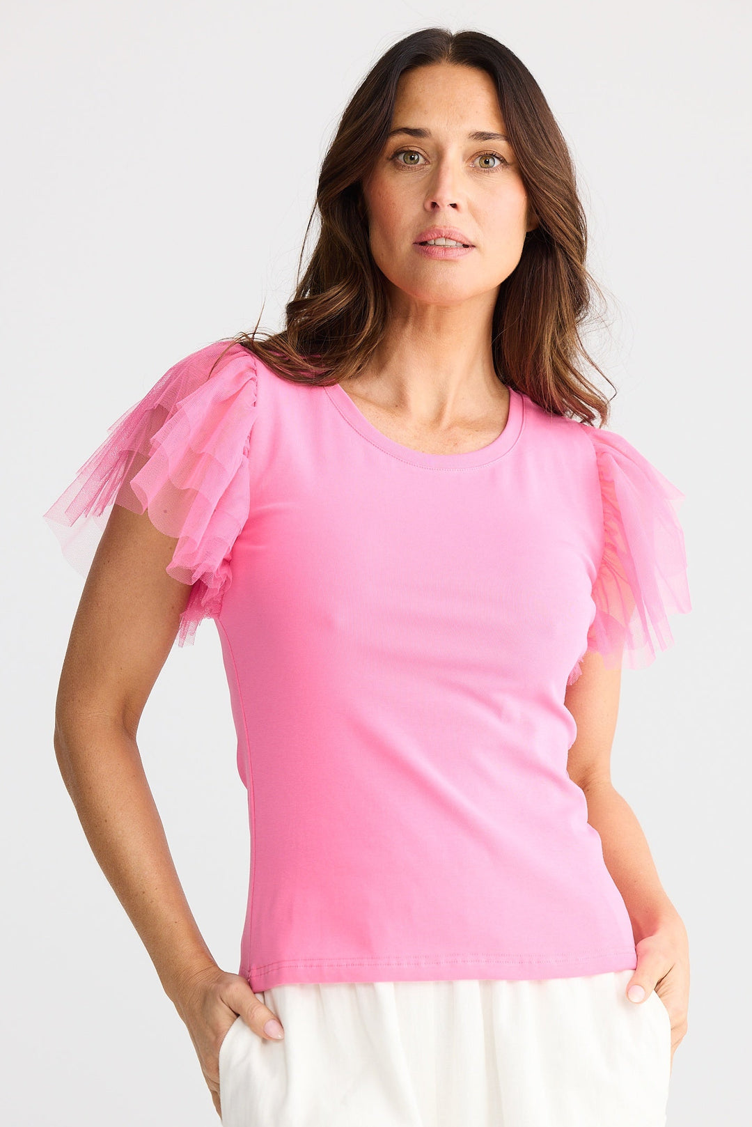 Woman wearing a pink brave & true chance tee with sheer sleeves on a white background