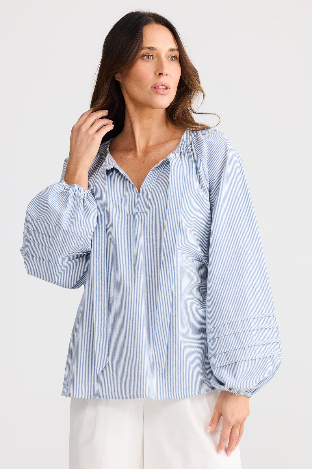 Woman wearing a light blue striped brave & true shirt and white shorts on a plain background