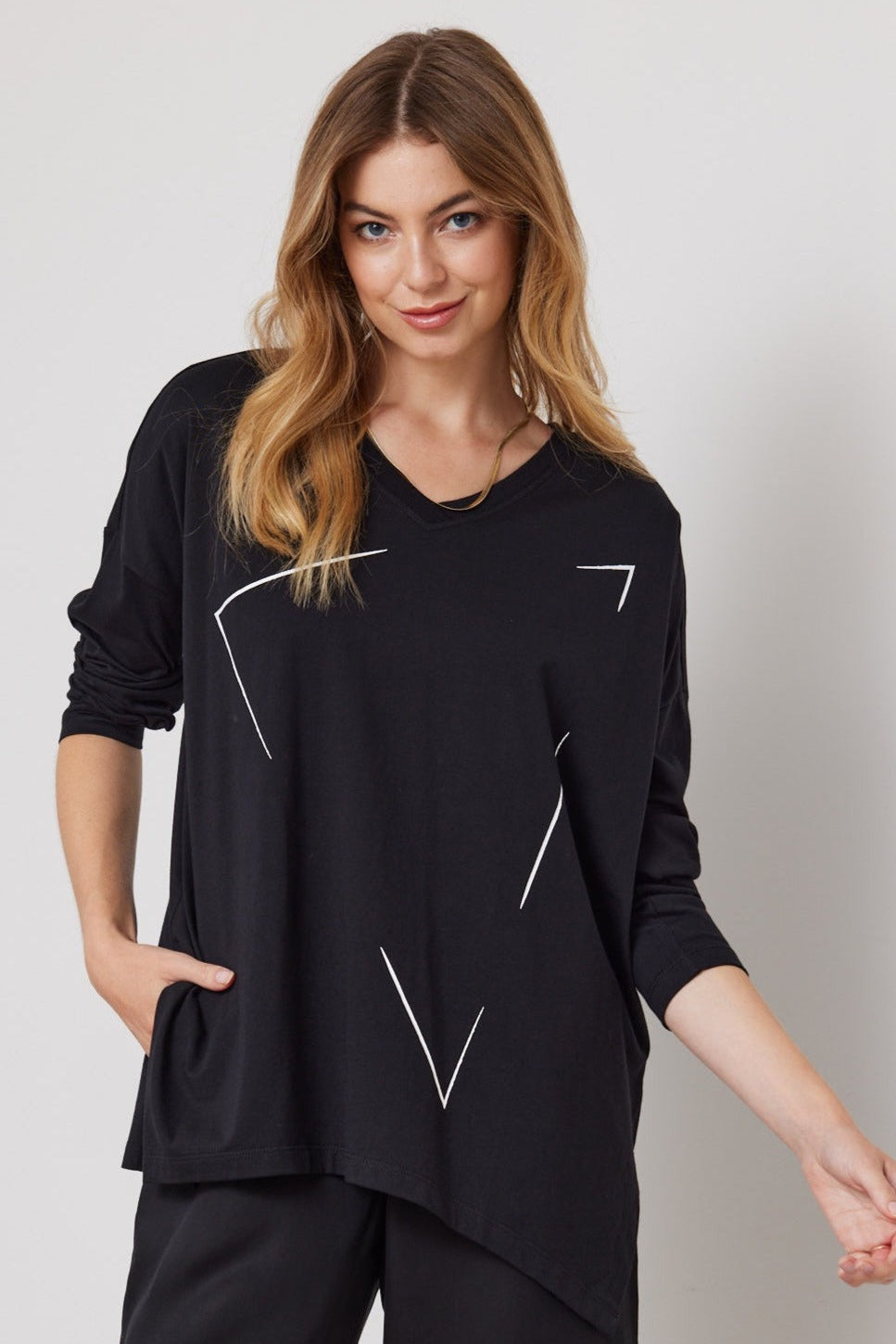A woman wearing a black V-neck tee with 3/4 sleeves and a geometric print at the front. The tee has a drop shoulder design.