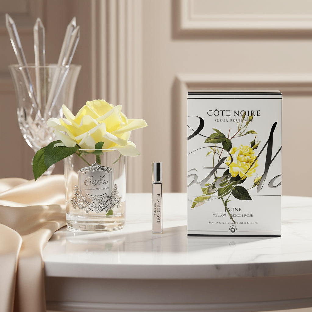 A life-like perfumed French Rose in a clear vase with a small bottle of scented perfume, packaging with 'Côte Noire' branding, and floral motifs.