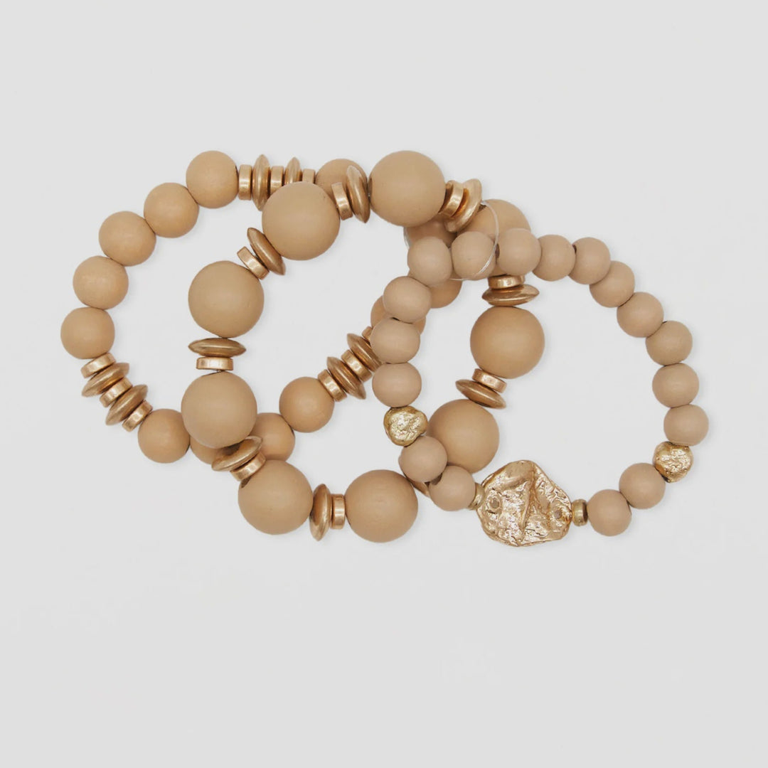Set of three beige beaded bracelets with gold accents on a light gray background