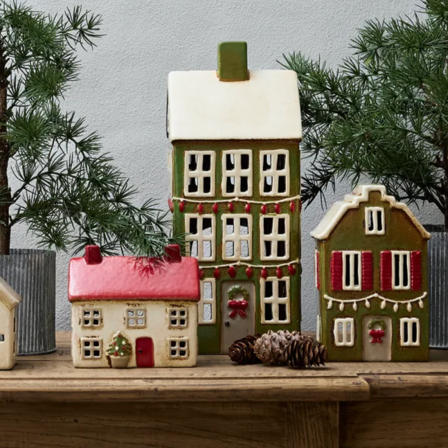 Decorative ceramic houses on a wooden surface with a gray background and pine trees.