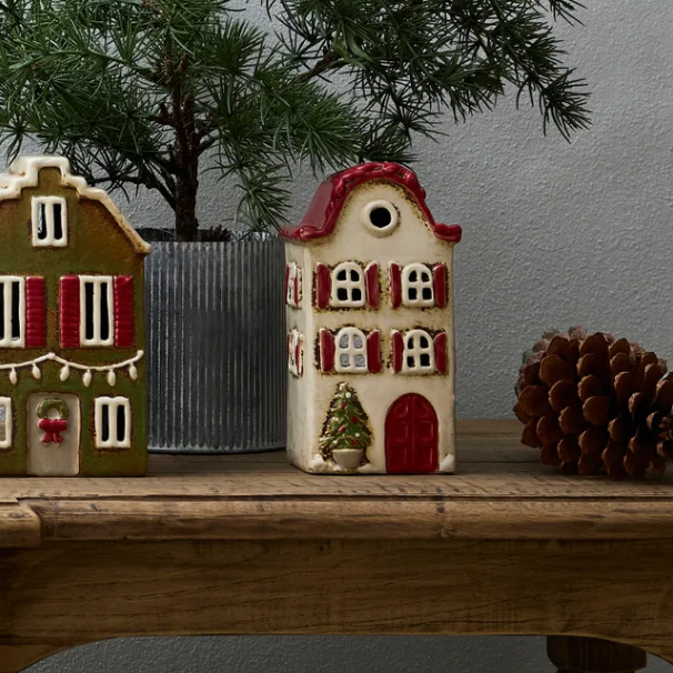Two small decorative houses on a wooden surface with a pine cone and tree branch in the background.