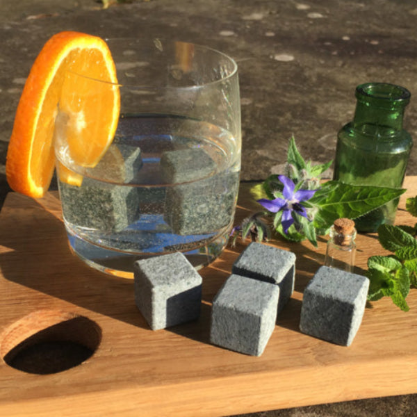 Glass of water with an orange slice, stones, and herbs on a wooden board.