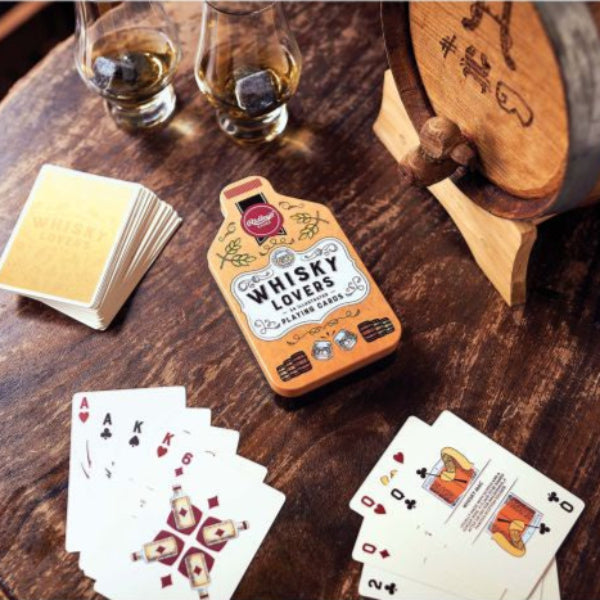 Playing cards with whisky-themed design on a wooden barrel with glasses of whisky.