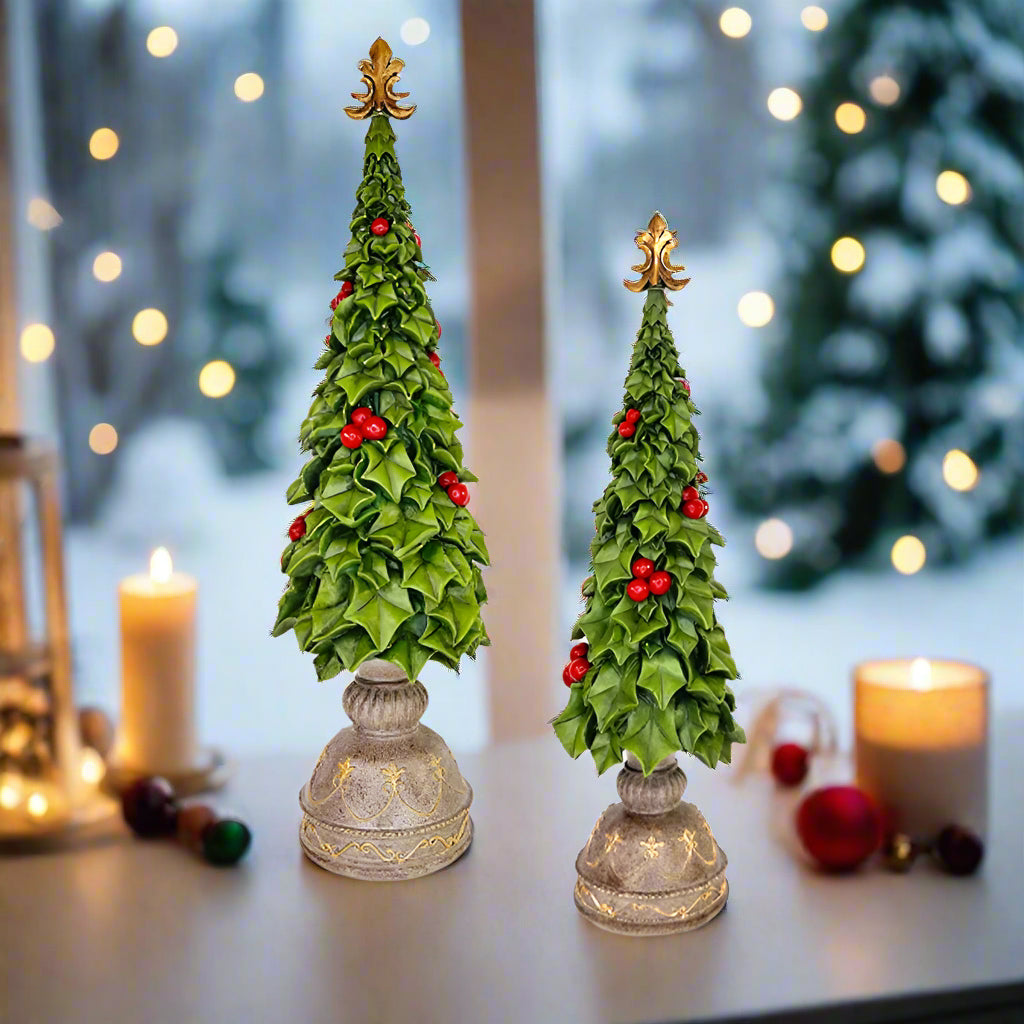 Two decorative Christmas trees with holly leaves and berries on a white background