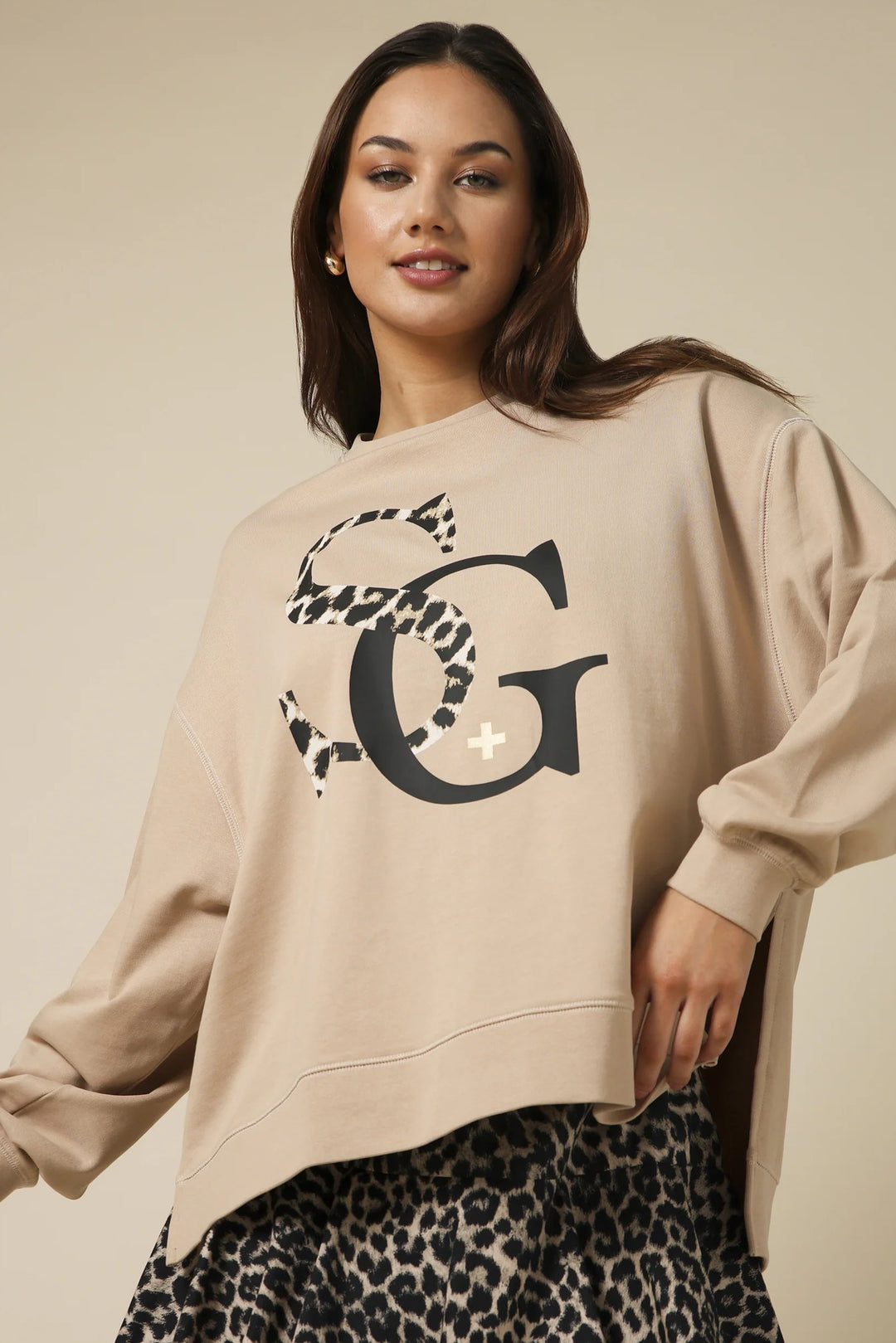 Woman wearing a beige sweatshirt with a large letter 'G' design on a beige background