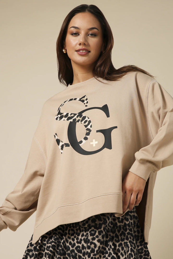 Woman wearing a beige sweatshirt with a large letter 'G' design on a beige background