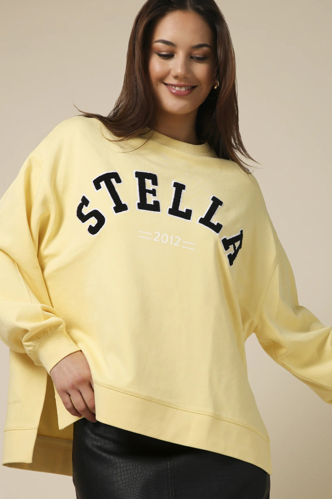 Woman wearing a yellow sweatshirt with 'STELLA' printed on it against a beige background