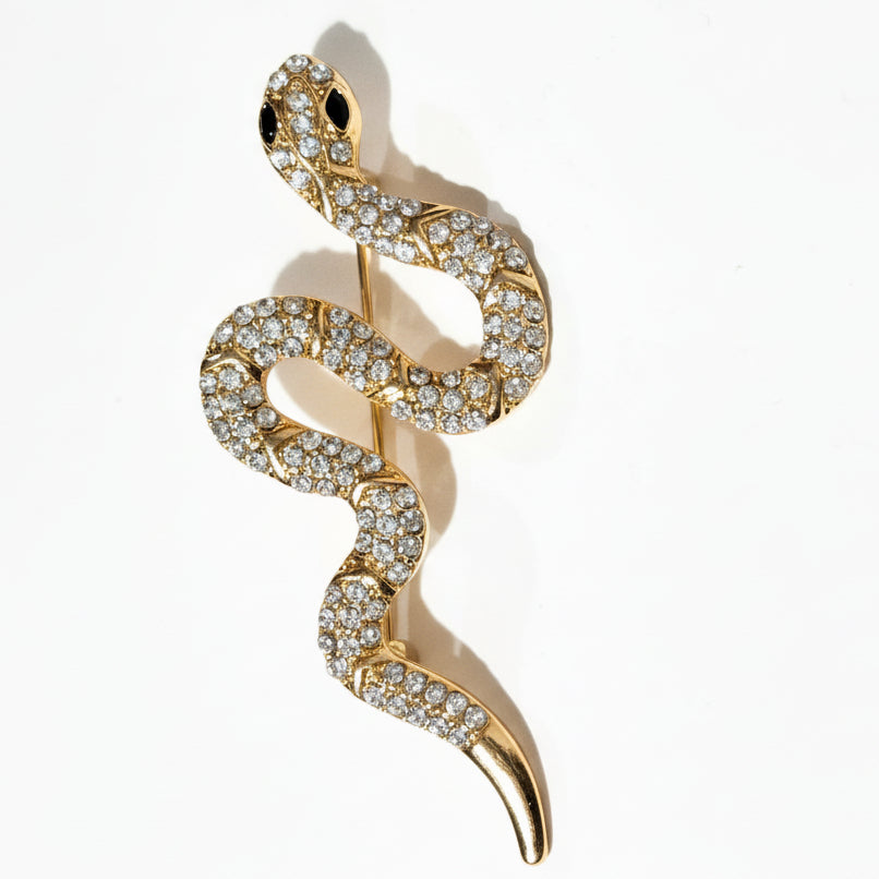 Gold snake-shaped pendant with embedded diamonds on a white background