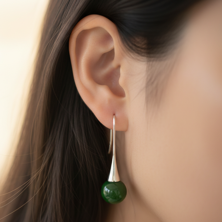 Greenstone teardrop earrings with silver hooks on a black stand.