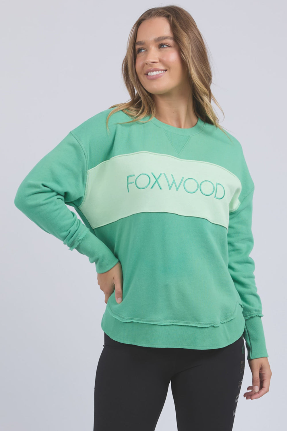 Woman wearing a green sweatshirt with 'FOXWOOD' logo and black shorts on a white background