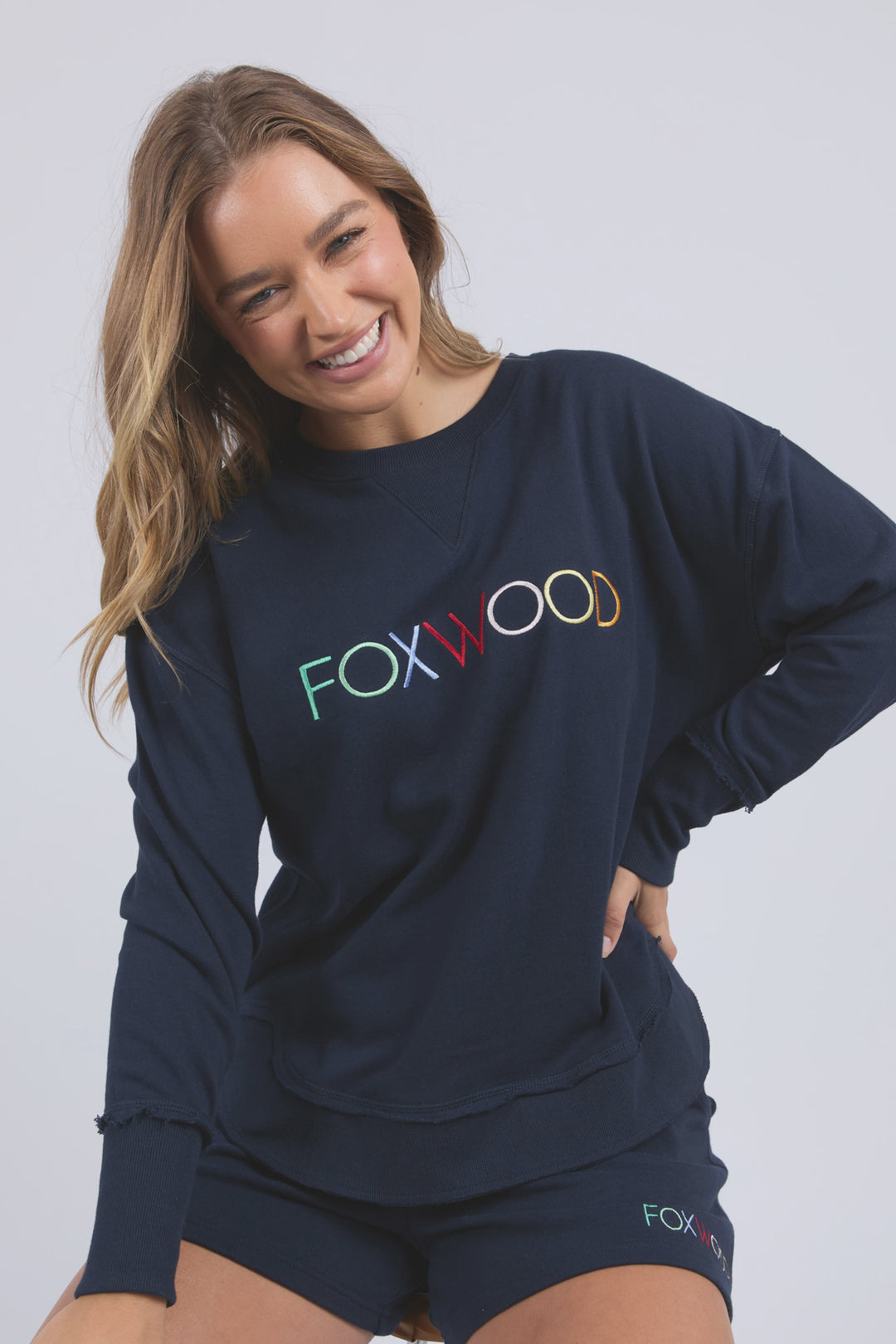Woman wearing a navy sweatshirt with 'FOXWOOD' printed on it against a plain background