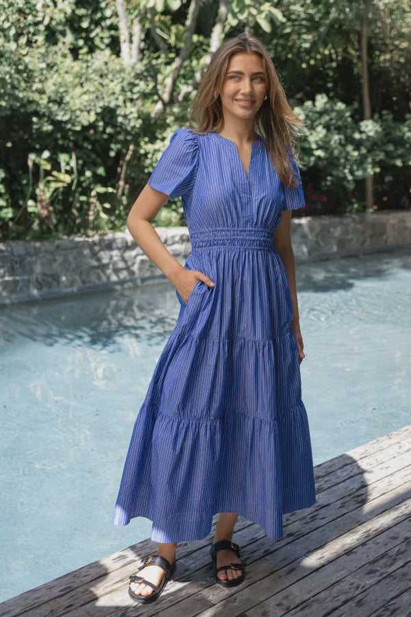 Woman in a blue dress standing by a pool with greenery in the background