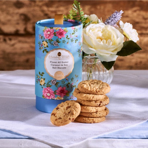 Biscuit tin with floral design, cookies, and flowers on a wooden surface