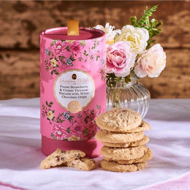 Pink floral candle with cookies and flowers on a white cloth