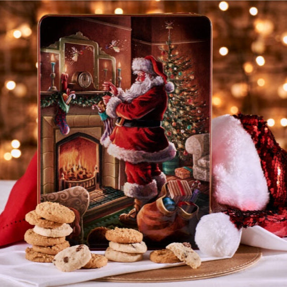 Decorative Christmas tin with Santa Claus by a fireplace, cookies, and a tree on a festive background.