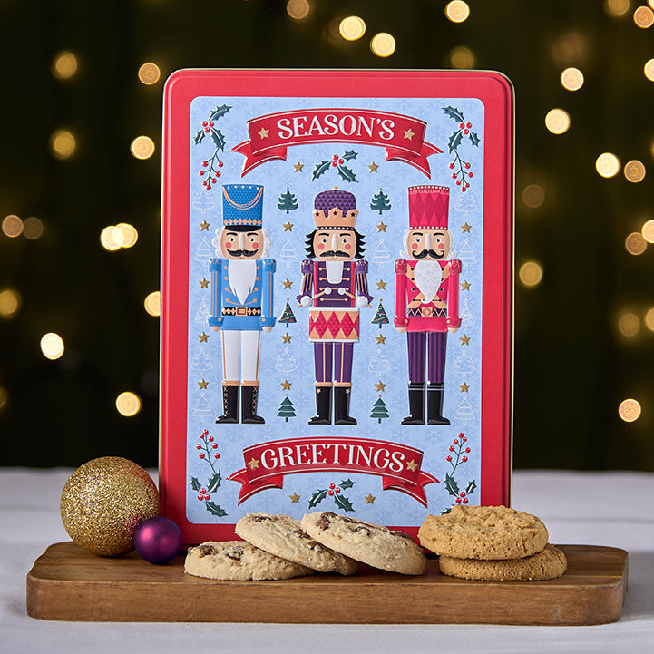 Decorative Christmas tin with nutcrackers and cookies on a wooden board against a festive background.