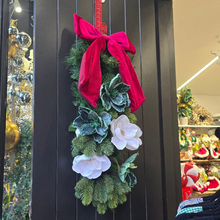 Decorative wreath with red bow and flowers on a black surface, possibly in a store setting.