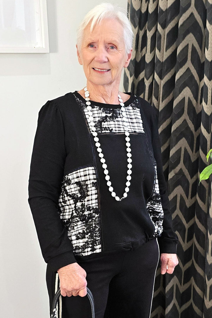 Woman in black outfit with white patterns holding a black handbag indoors.