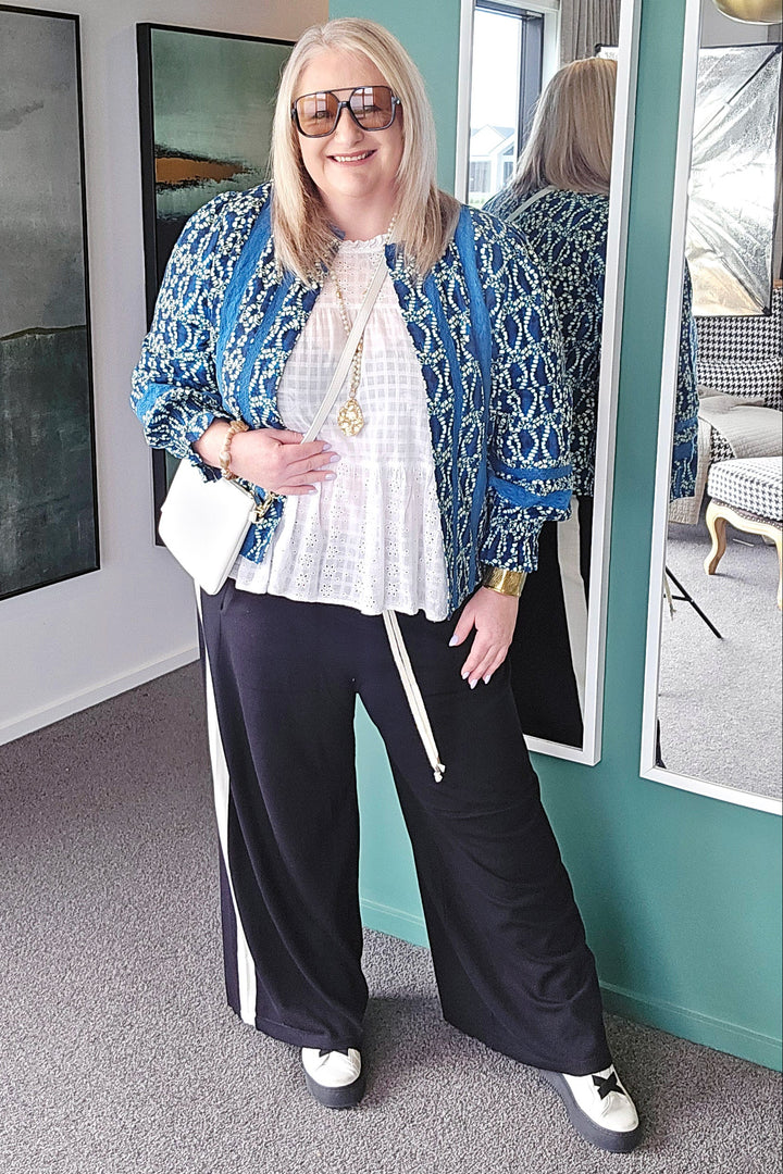 Woman standing in a room with teal walls, wearing a blue jacket and black pants.