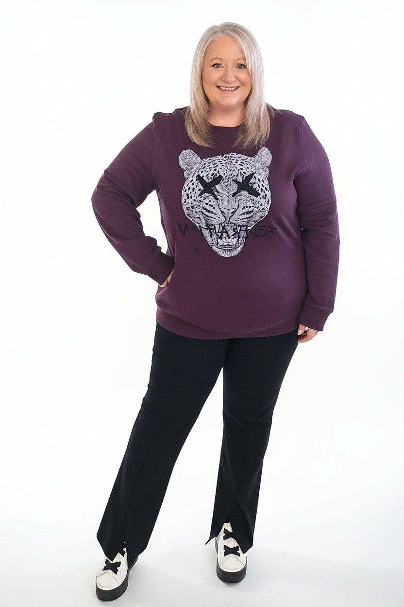 Woman wearing a purple sweatshirt with a graphic design, standing indoors.