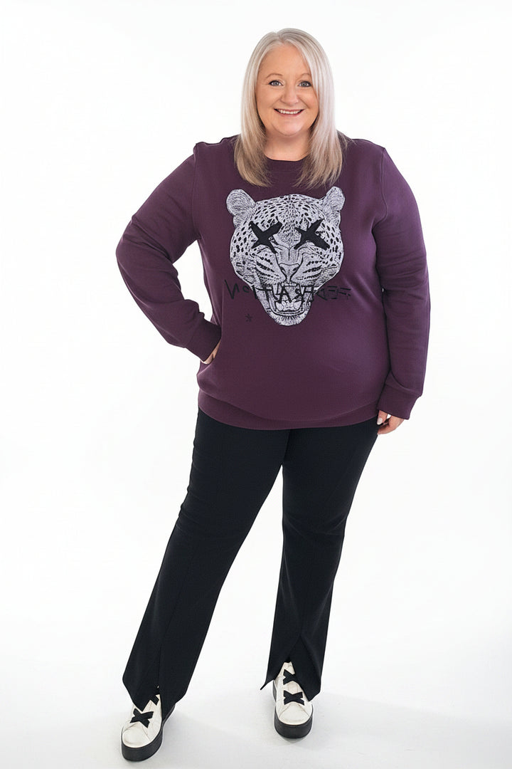 Woman wearing a purple sweatshirt with a graphic design, standing indoors.