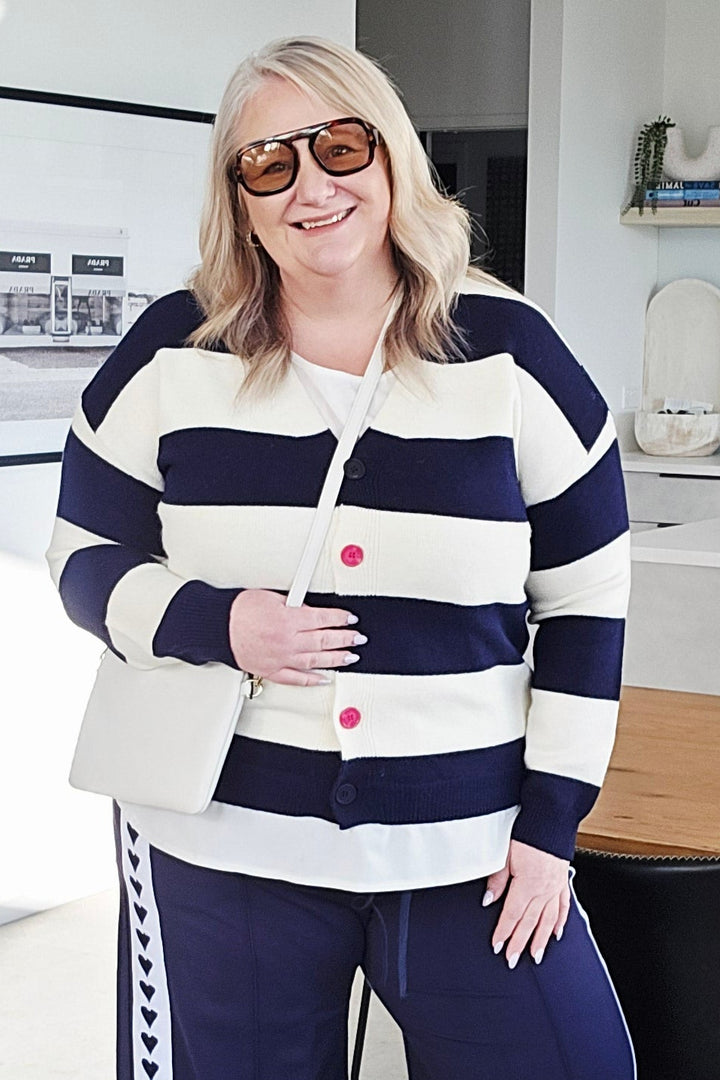 A woman modeling a navy blue and white striped knit sweater and matching wide-leg pants with white sneakers in a modern office setting.