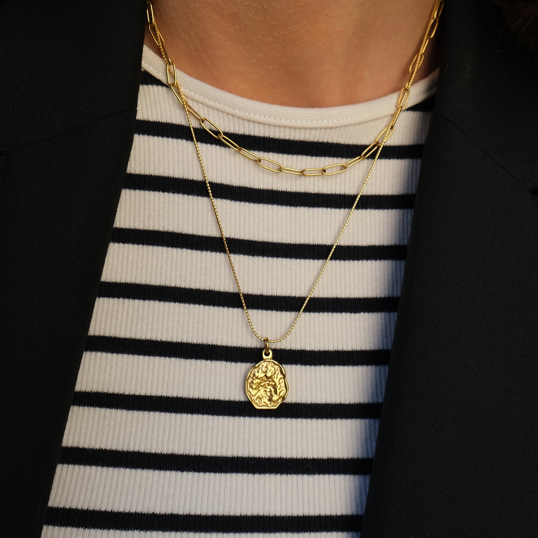 Gold necklace with a pendant on a black and white striped shirt against a dark background