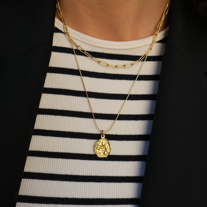Gold necklace with a pendant on a black and white striped shirt against a dark background