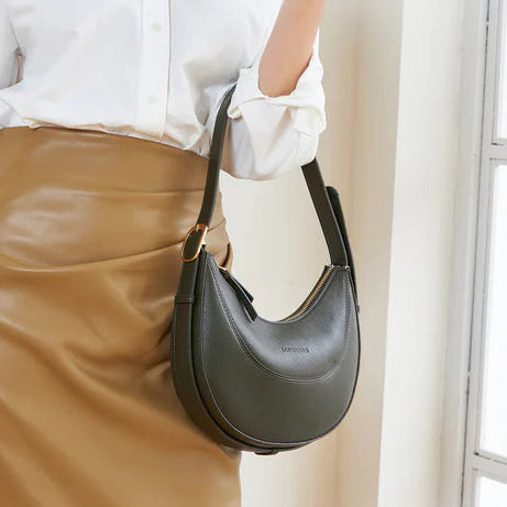 Woman holding a black handbag wearing a white shirt and brown skirt indoors.