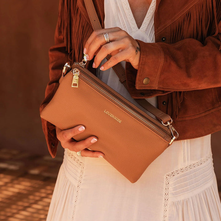 Person holding a brown leather bag with 'LOVEVOOK' branding, wearing a brown jacket and white dress.