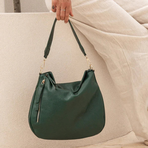 Green handbag held by a person wearing light-colored pants against a neutral background