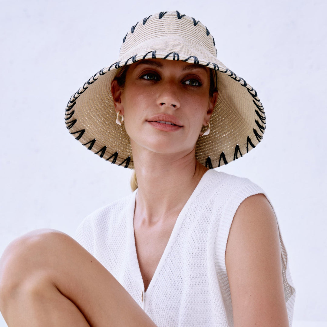Woman wearing a white dress and straw hat sitting on a white surface with a blurred outdoor background