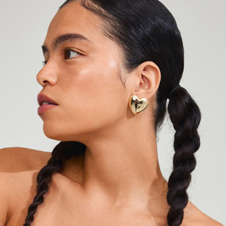 Woman with braided hair wearing a white off-shoulder top against a plain background