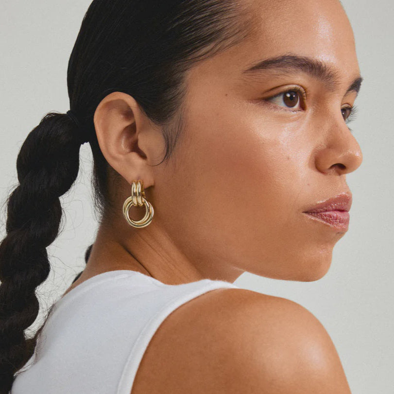 Woman with a braid wearing gold hoop earrings against a neutral background