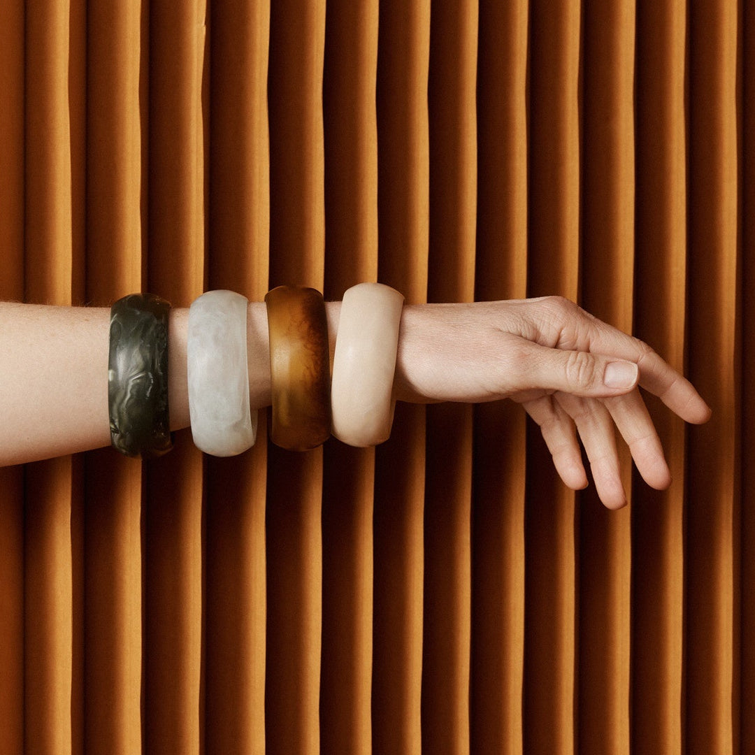 Hand with bracelets reaching out from behind a brown pleated curtain