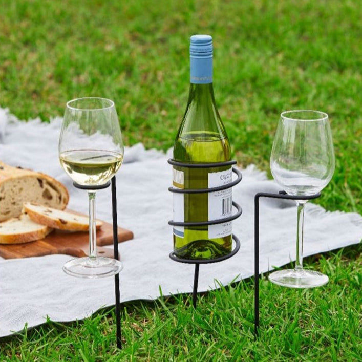 Wine bottle holder with two glasses on a picnic blanket outdoors